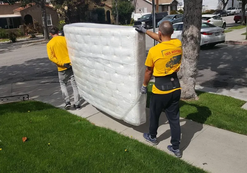 Professional moving crew carry a wrapped queen size mattress. Trek Movers is full-service, long distance moving company.