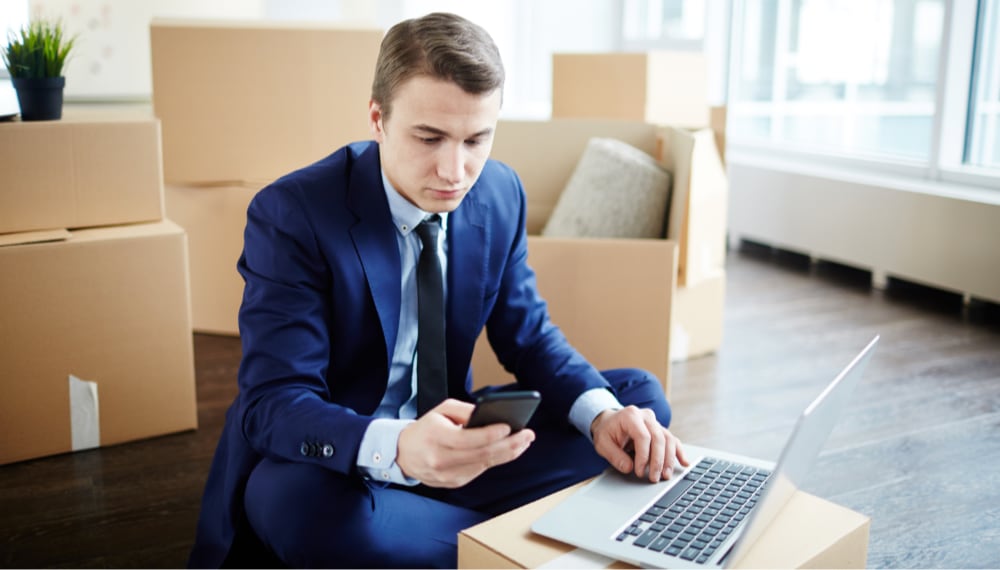 Man sitting among moving boxes using a laptop, TrekMovers