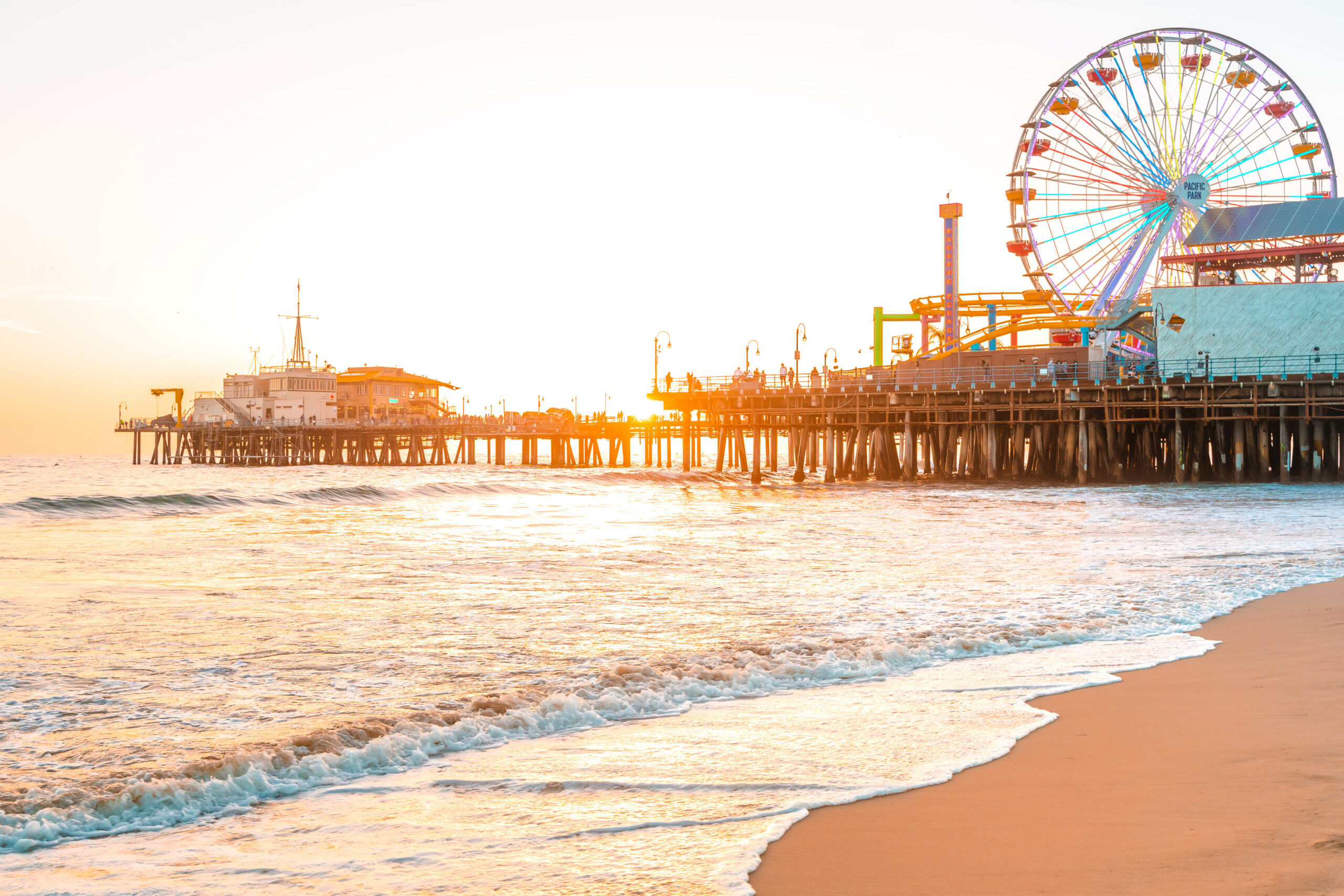 Santa Monica Pier against the background of an orange sunset and calm ocean waves in Los Angeles, California.