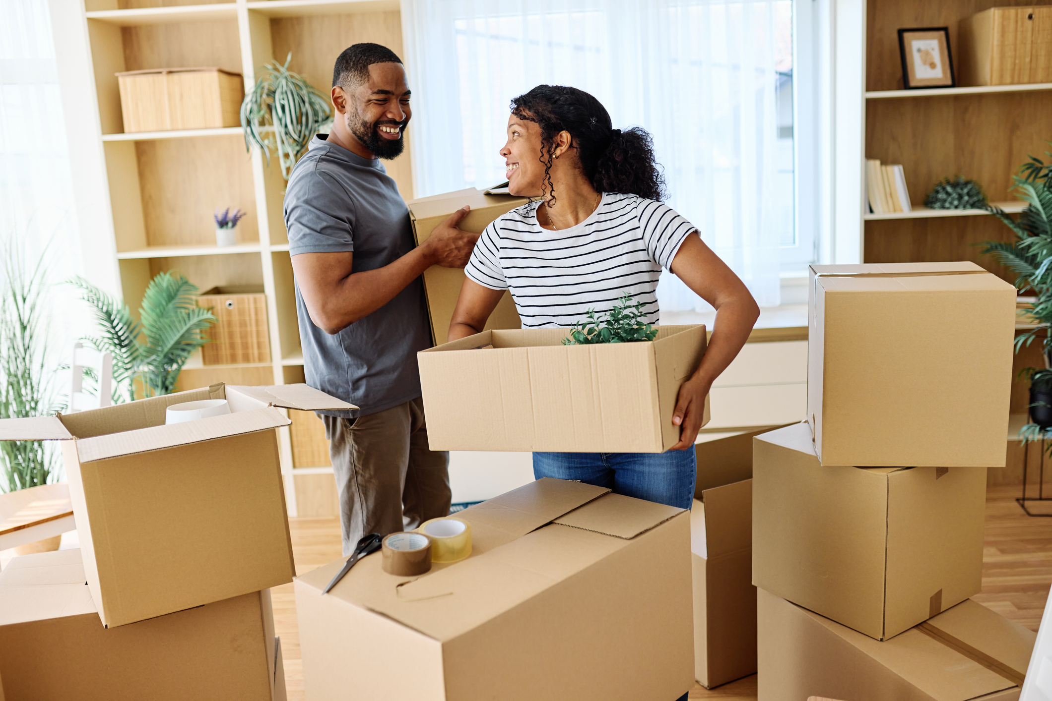 Young couple moving out of their L.A. apartment, carrying boxes together.
