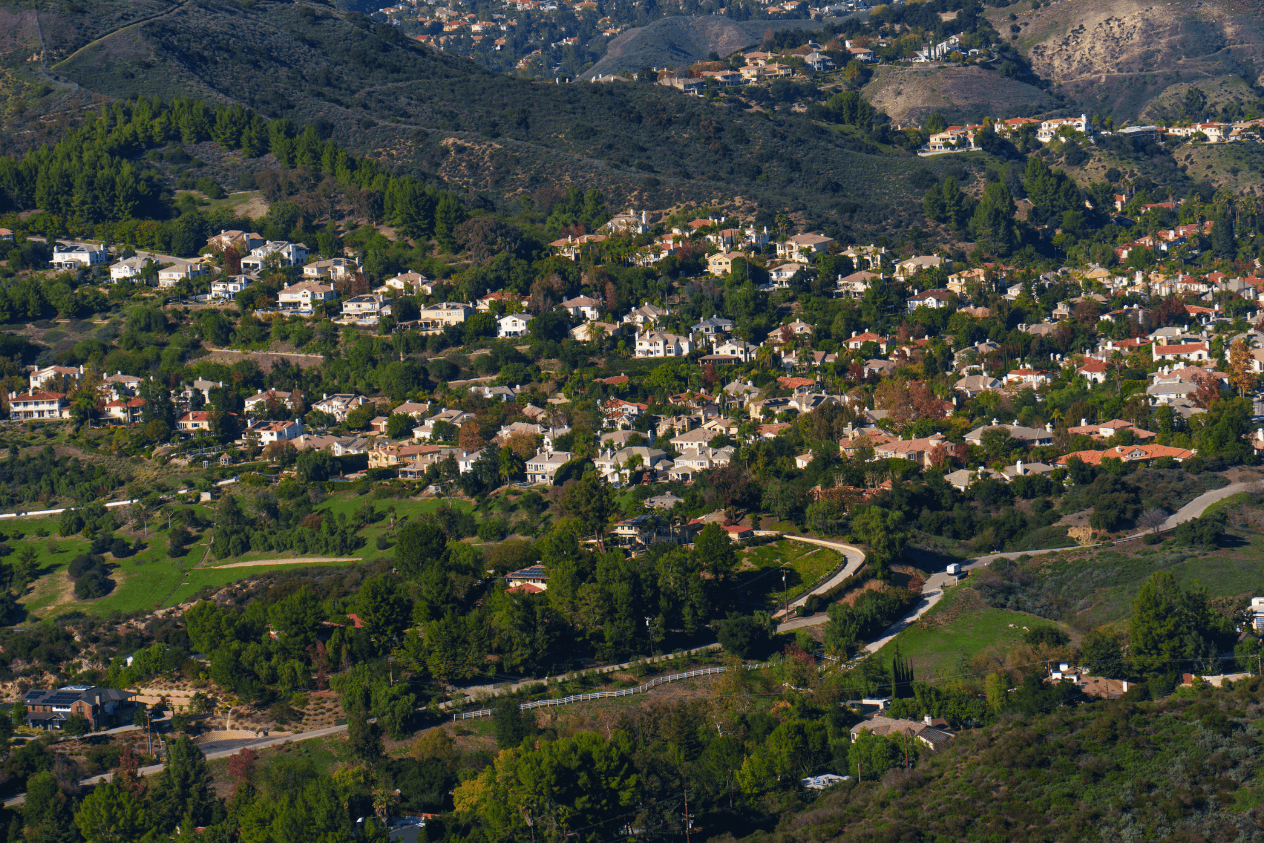 Numerous luxury residences are gracefully integrated into the undulating, tree-covered hills of Calabasas, Los Angeles, showcasing a desirable, scenic suburban landscape.